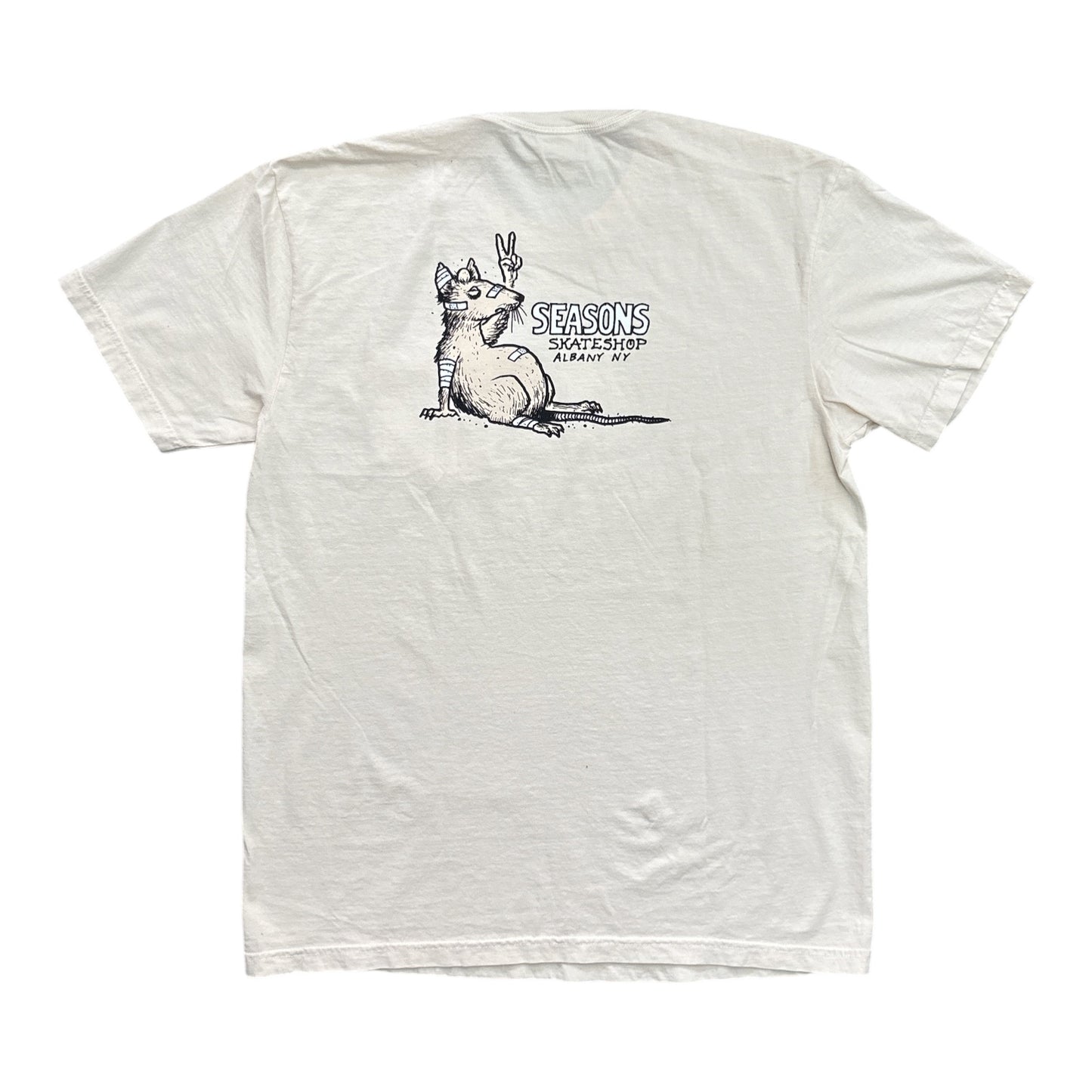 An off-white short-sleeve t-shirt with a black graphic print on the chest showing a cat making a peace sign and the text 'SEASONS SKATESHOP SAN ANTONIO'.