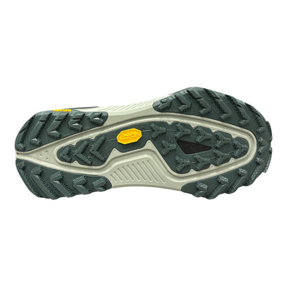 A close-up of a hiking shoe's outsole, showing a dark green and off-white tread pattern with two yellow Vibram logos, isolated on a white background.