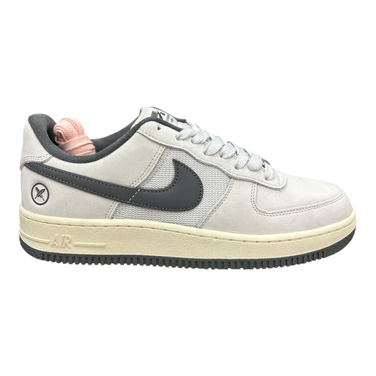 A low-top Nike sneaker in light gray suede and mesh with a dark gray Swoosh, a cream midsole, and a pink extra set of laces