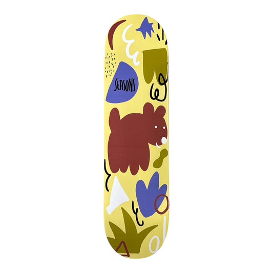 A skateboard deck featuring a whimsical, hand-drawn style illustration on a pale yellow background. The design includes a brown bear, blue and olive green shapes, and the 'SEASONS' brand logo.