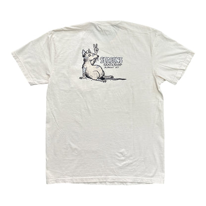 An off-white short-sleeve t-shirt with a black graphic print on the chest showing a cat making a peace sign and the text 'SEASONS SKATESHOP SAN ANTONIO'.