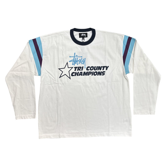 A vintage long-sleeve triathlon shirt by Stüssy, featuring a white body, navy blue collar and 'TRI COUNTY CHAMPIONS' text, light blue and navy stripe details on the sleeves, and a Stüssy logo.