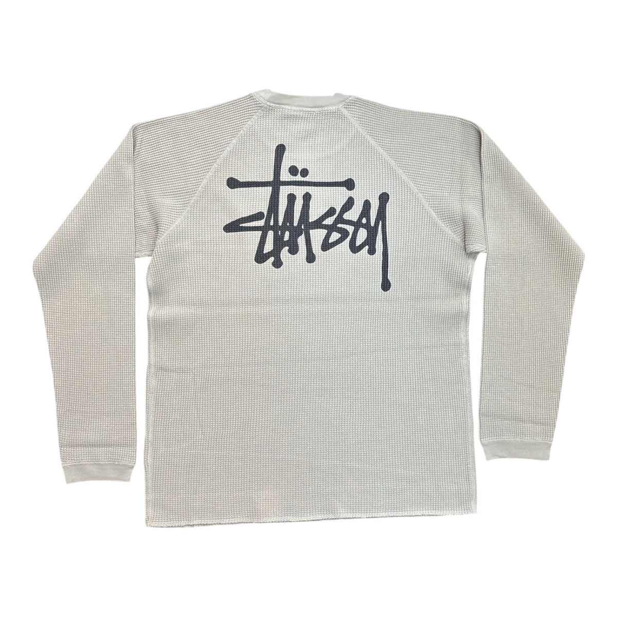A Stüssy waffle-knit raglan long-sleeve shirt in light gray, featuring the brand's signature script logo printed in black across the back.